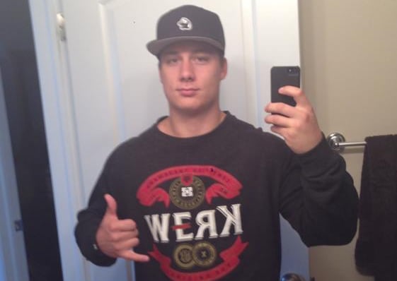 A man in a black cap takes a selfie in a mirror while making a hand gesture.