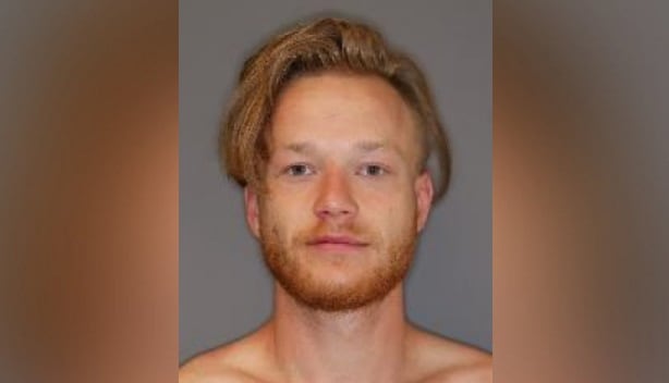 A shirtless man with a red beard in front of a grey background.