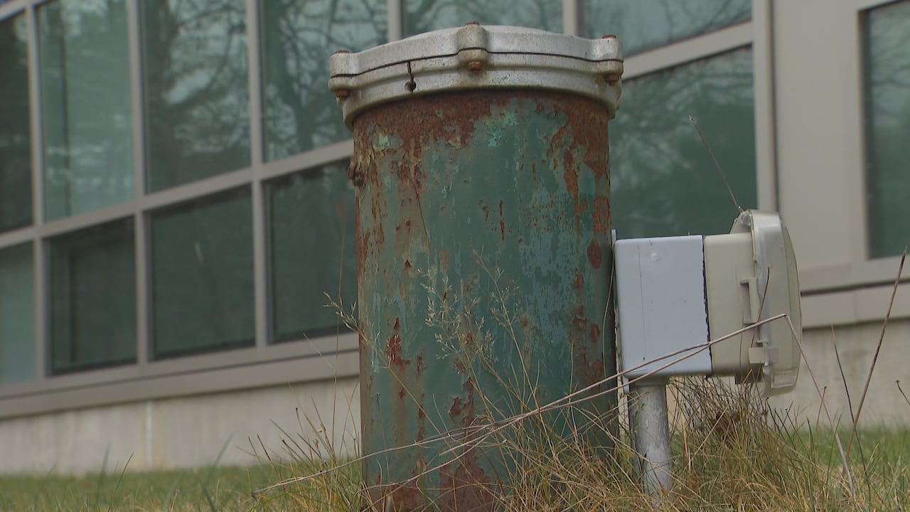 Green rusting well pipe in the lawn in front of a building.