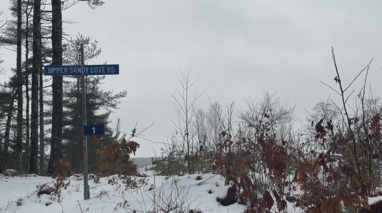 A street sign is seen in a rural area with snow on the ground. 