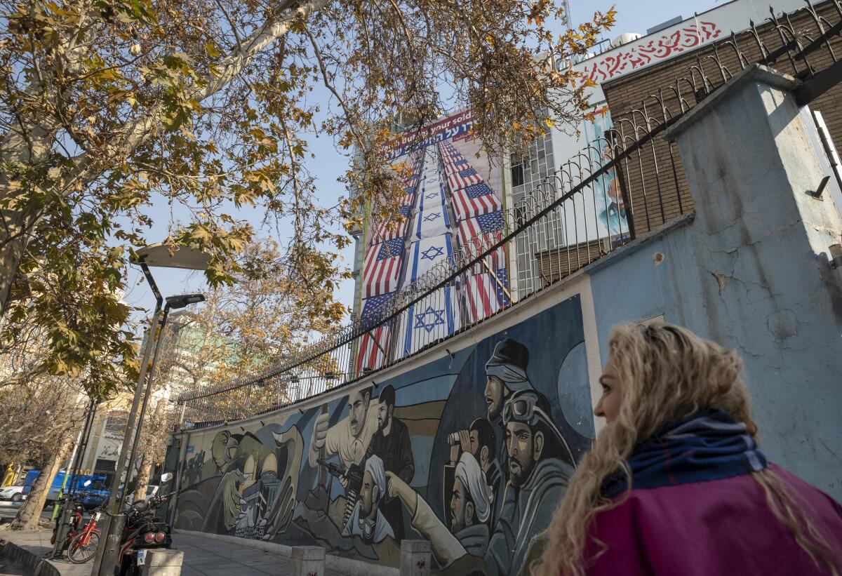A young Iranian woman walks under an anti-U.S. and Israeli billboard