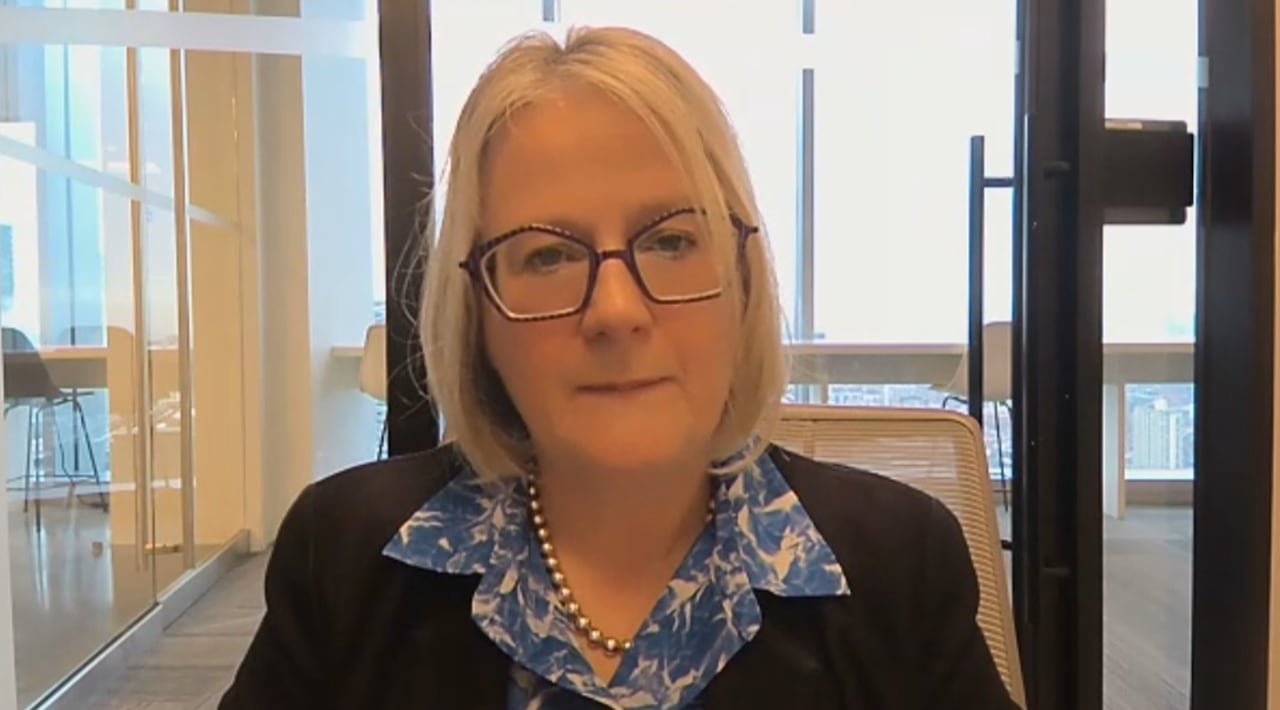 A woman with blonde hair wearing glasses and a dark blazer with a blue and white blouse