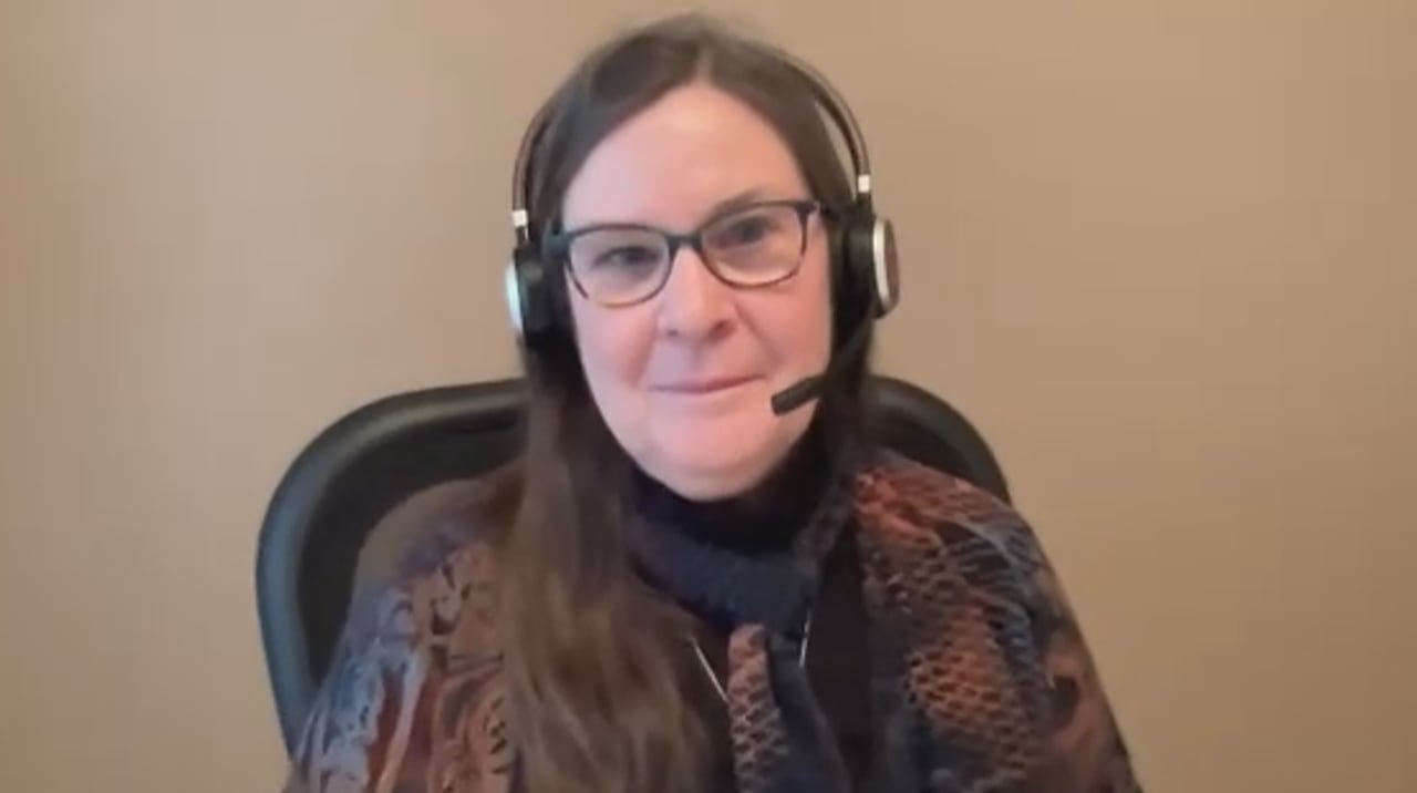 A woman with dark hair, wearing a black shirt and glasses and a headset.