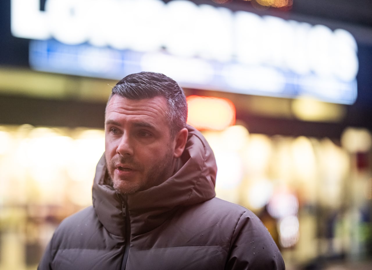 A white man wearing a grey puffer jacket is seen outside a retail outlet that reads 'London Drugs'.