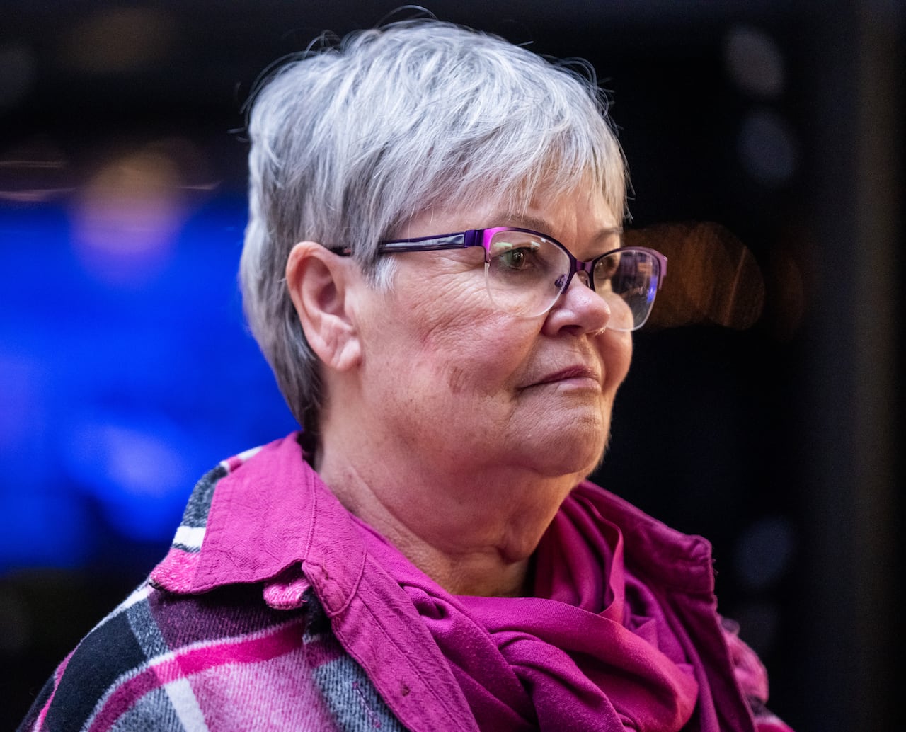 A woman with short white hair and wearing a pink top.