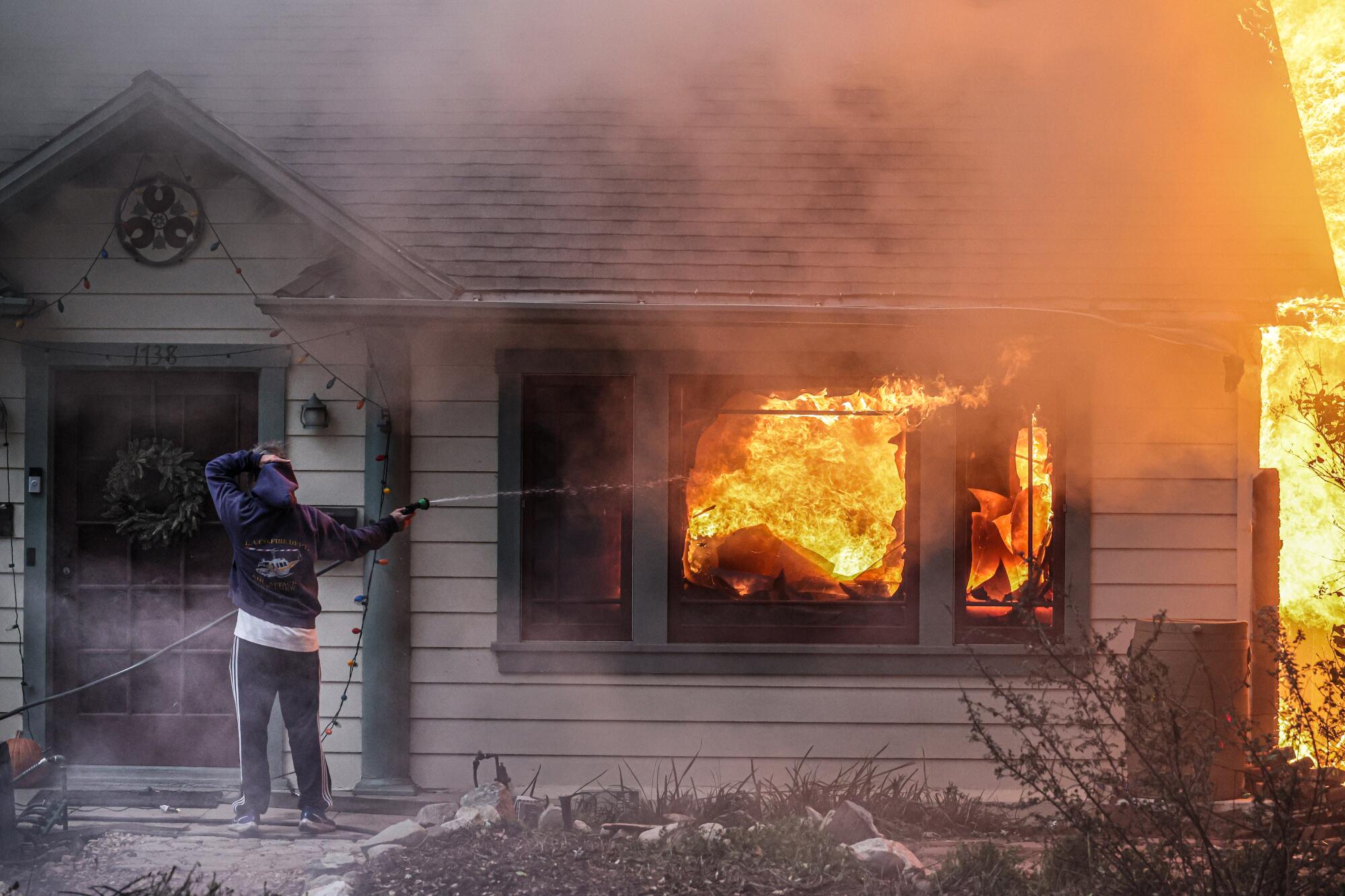 A man points a water hose at a burning house