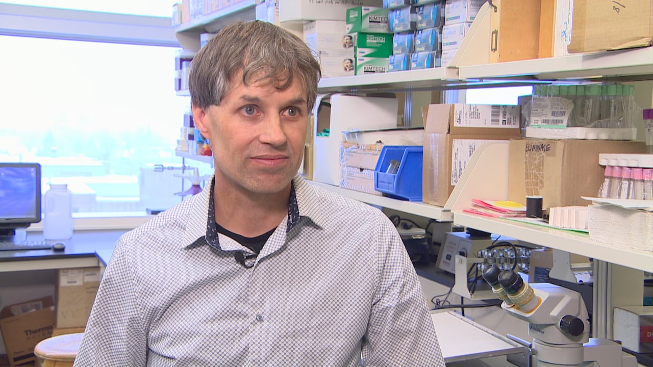 A man sits in an office with medical equipment and supplies on shelves behind him.