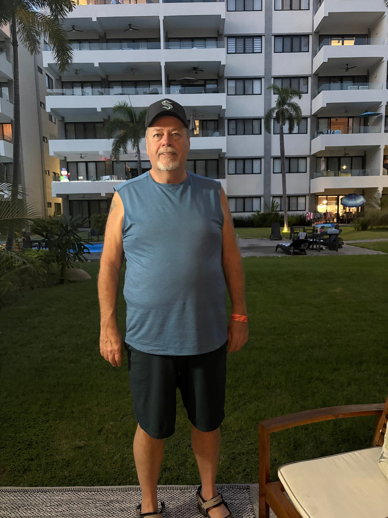A white man in a black hat standing in a blue tank top and black shorts. 