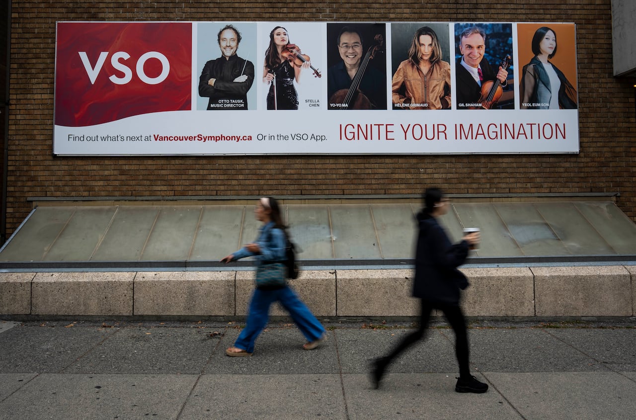 People walk by a sign featuring orchestra musicians and the words 'VSO Ignite your imagination'.