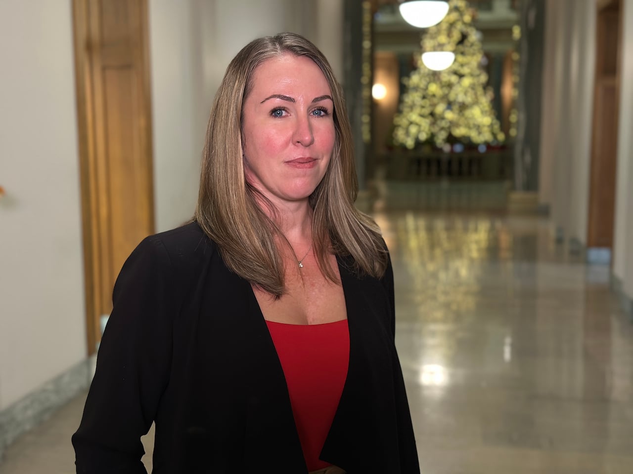 A woman wearing a red shirt with a black blazer poses for a photograph.