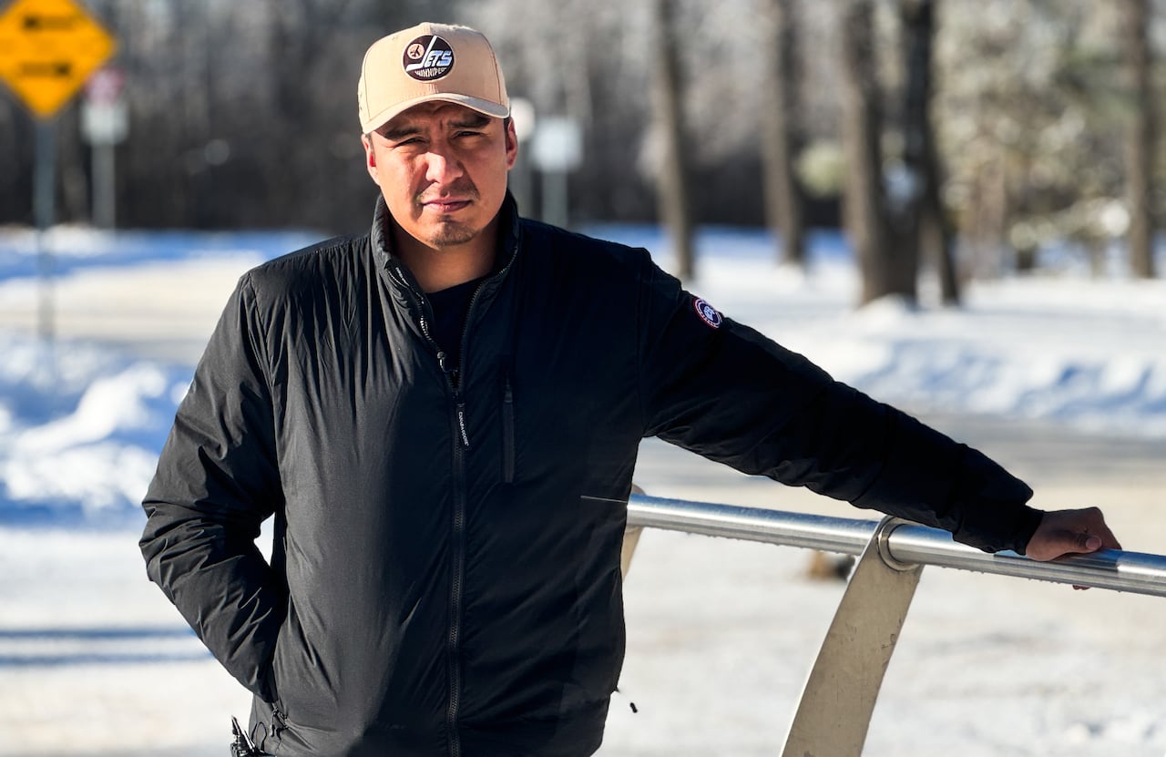 A man in a black jacket and Winnipeg Jets ball cap stands outside in winter.