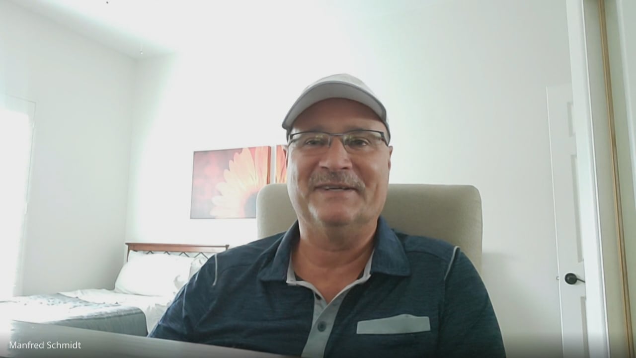 A man in a blue shirt sits in a bedroom.