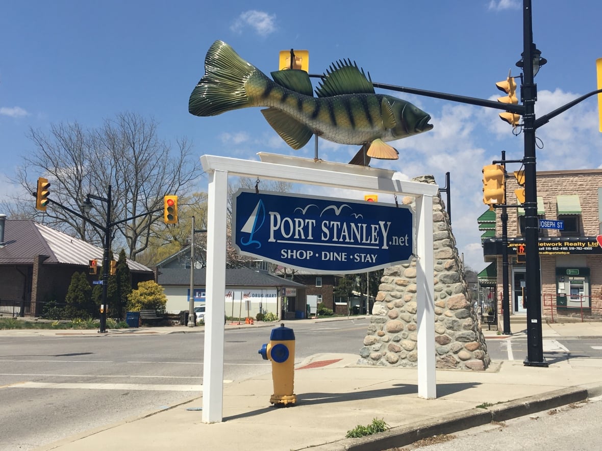 A sign in the core of Port Stanley Ontario on a sunny day. The sign is topped by a large model of a fish.