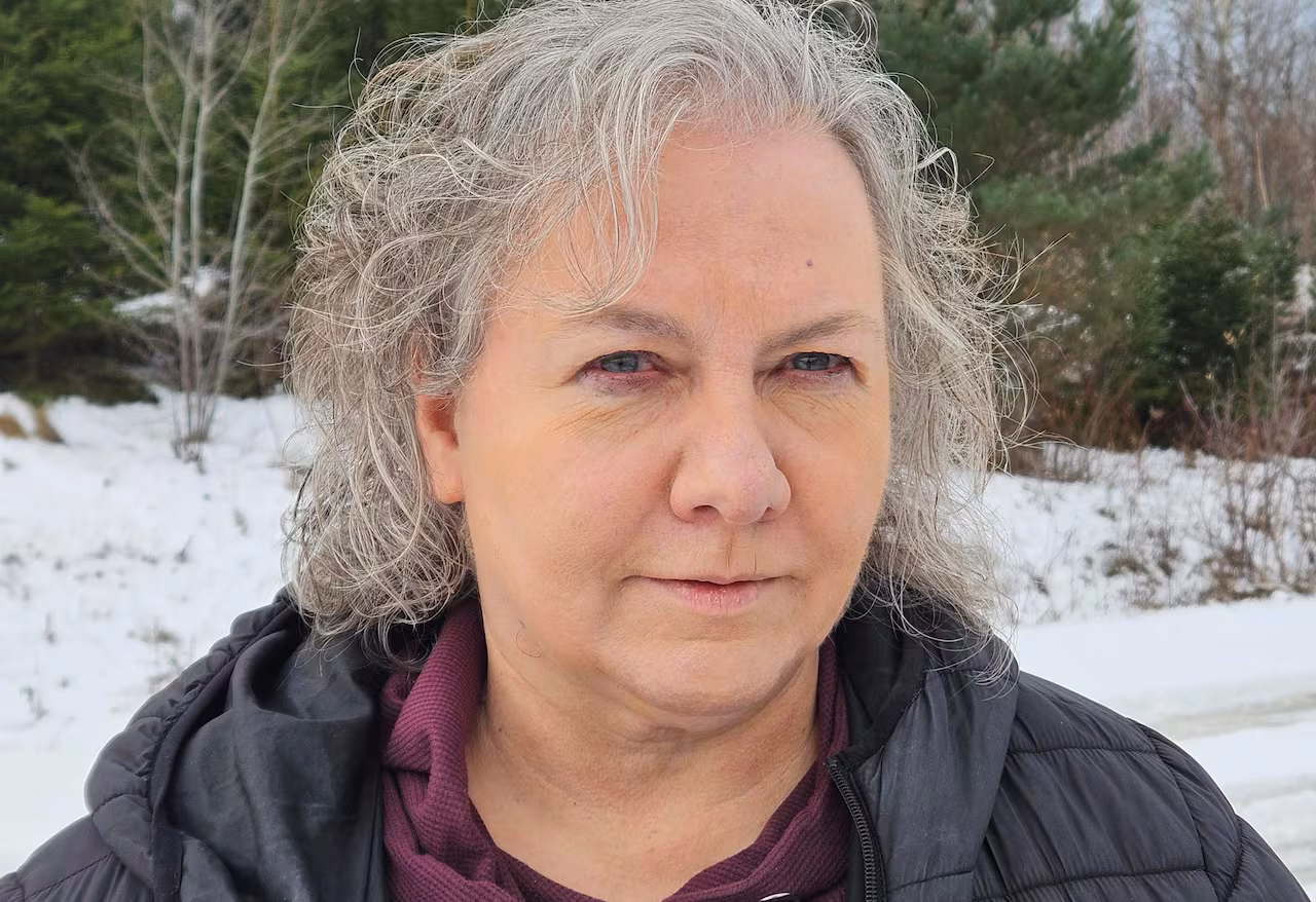 Kim Jensen stands outside in a wooded area.