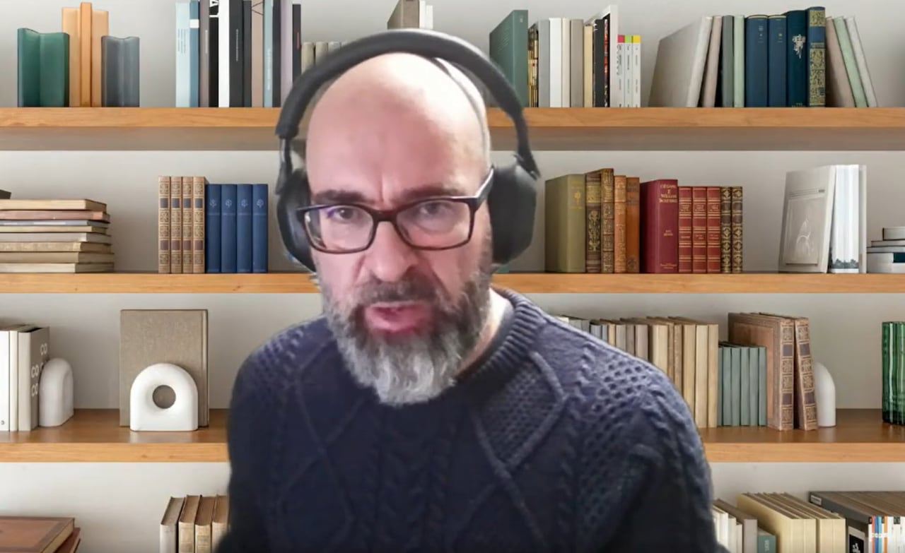 A bearded man with a sweater wearing headphones on a video chat. 