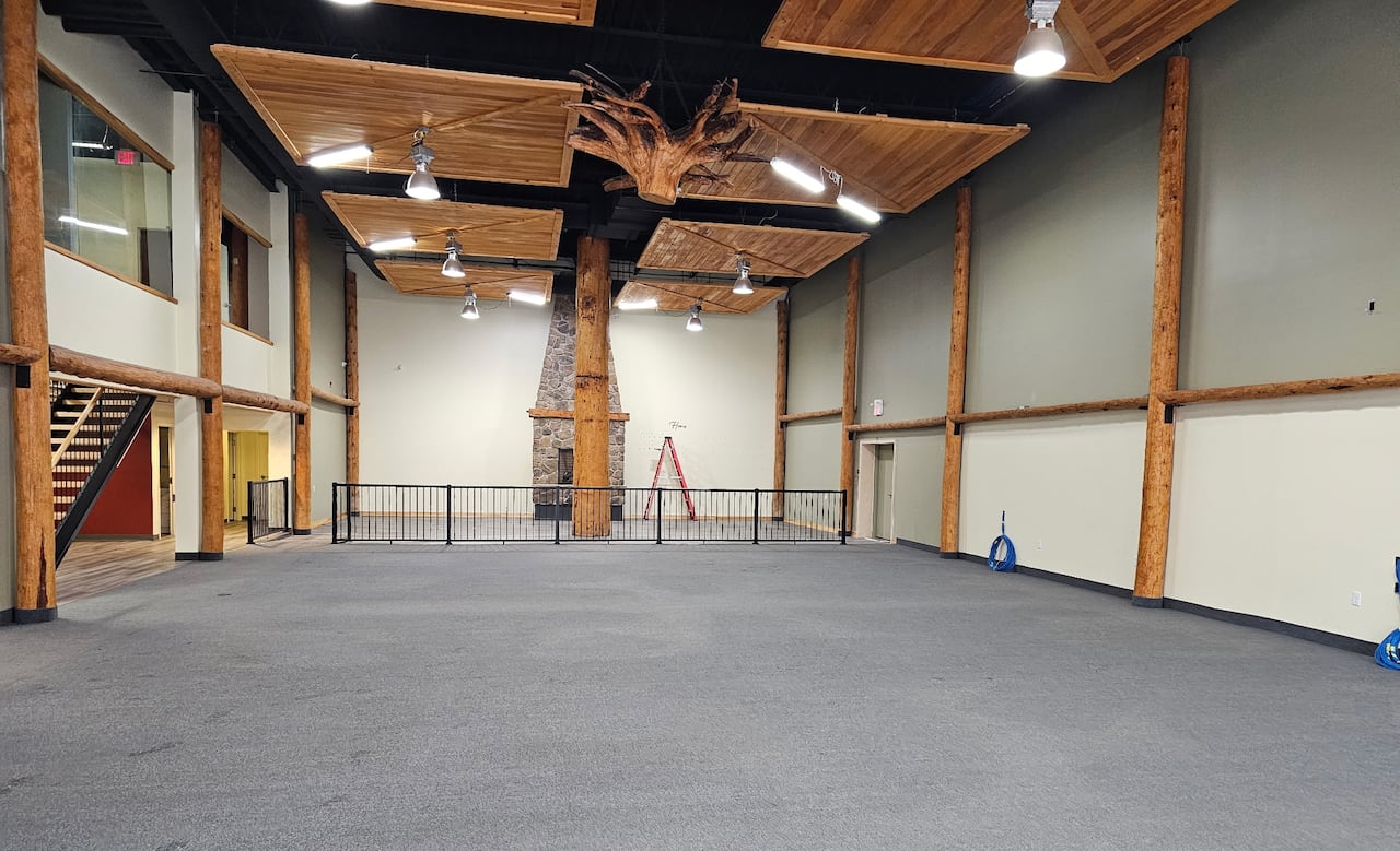 Wide shot of a large room with grey carpet and exposed wood beams