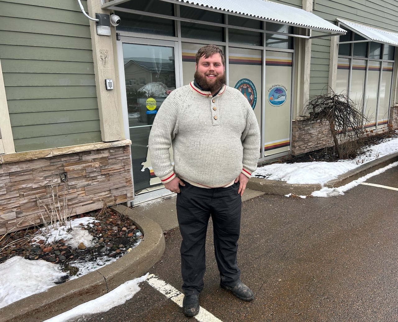 A young man with brown hair stands outside of a building with green siding