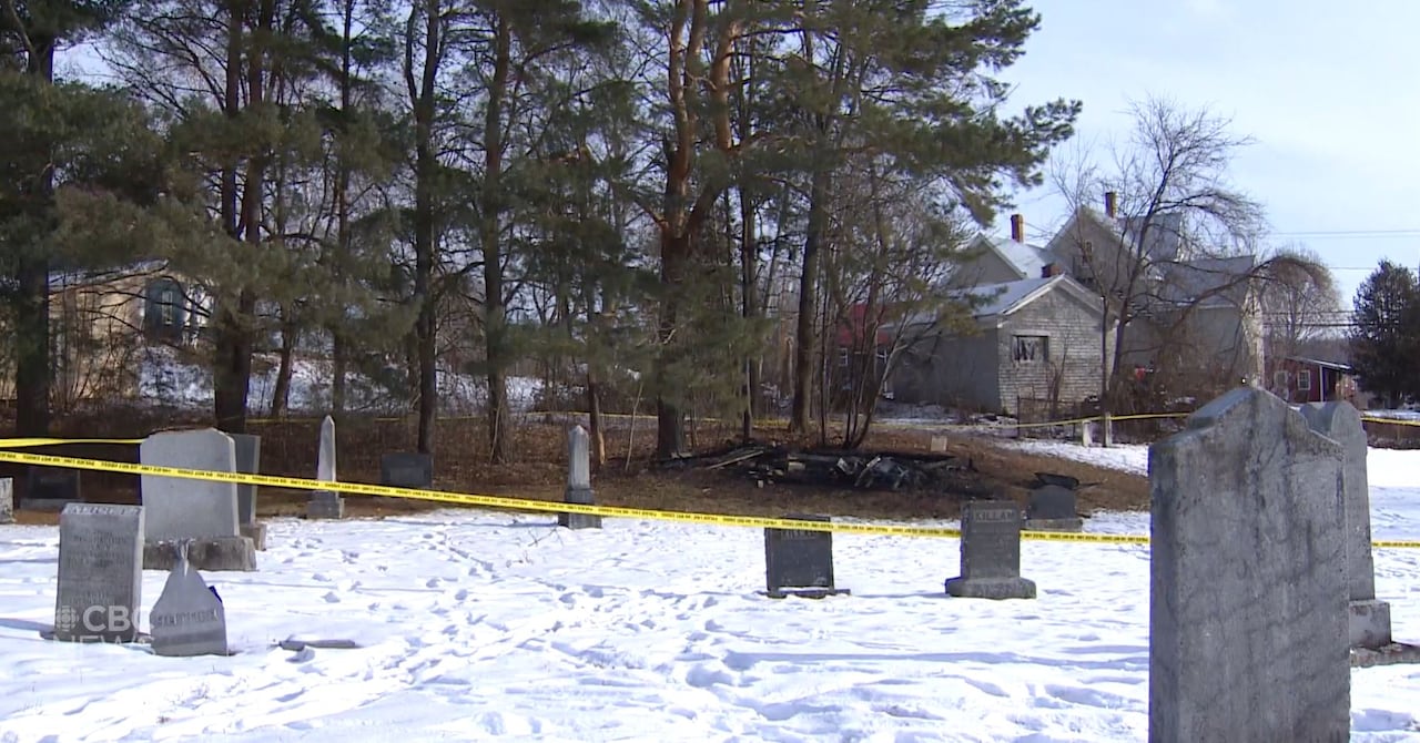 Police tape and the charred remains of a backyard shed with houses in the background.