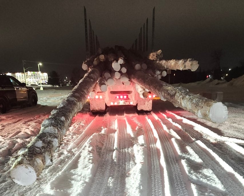 A truck with long logs sticking out the back.