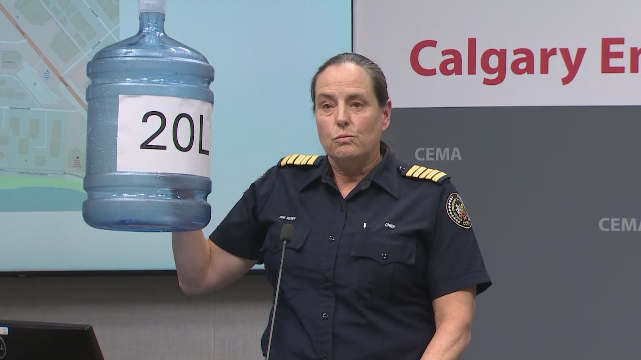 A woman in uniform holds up an empty water jug with a piece of paper that reads 20L on it