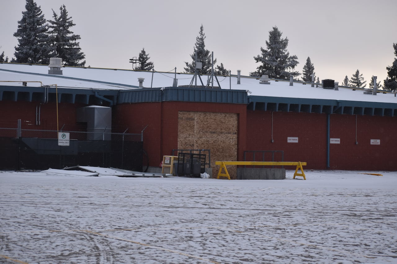 A brick building pictured on a winter day with plywood covering a garage door size entrance.
