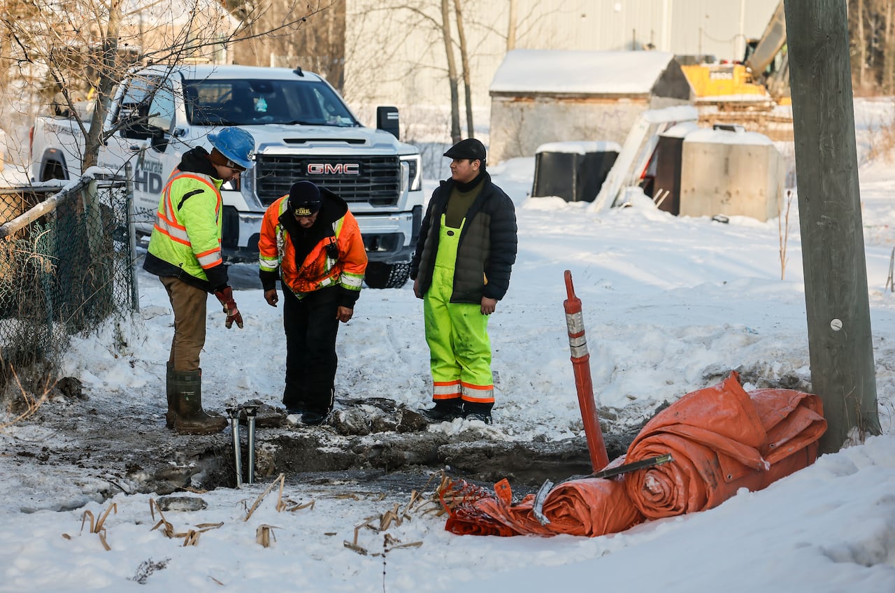 Workers in yellow and orange vest look down to inspect a water main break in front of a home.