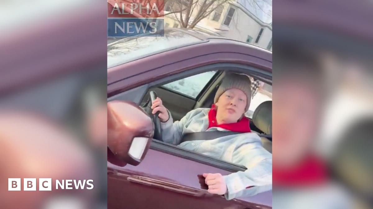 A woman wearing a sleeveless, yellow textured top, seated in front of a mirror with round vanity lights in a dressing room setting.