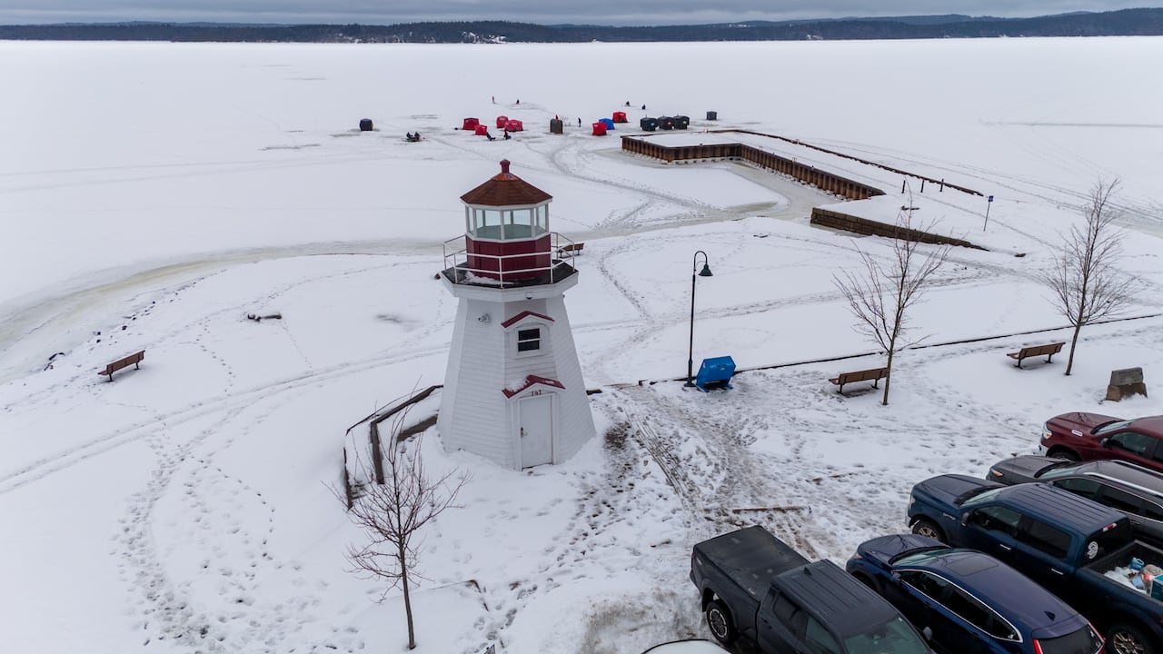 An aerial view of a lighthouse and a wharf, with a small ice-fishing village and open river in the background.