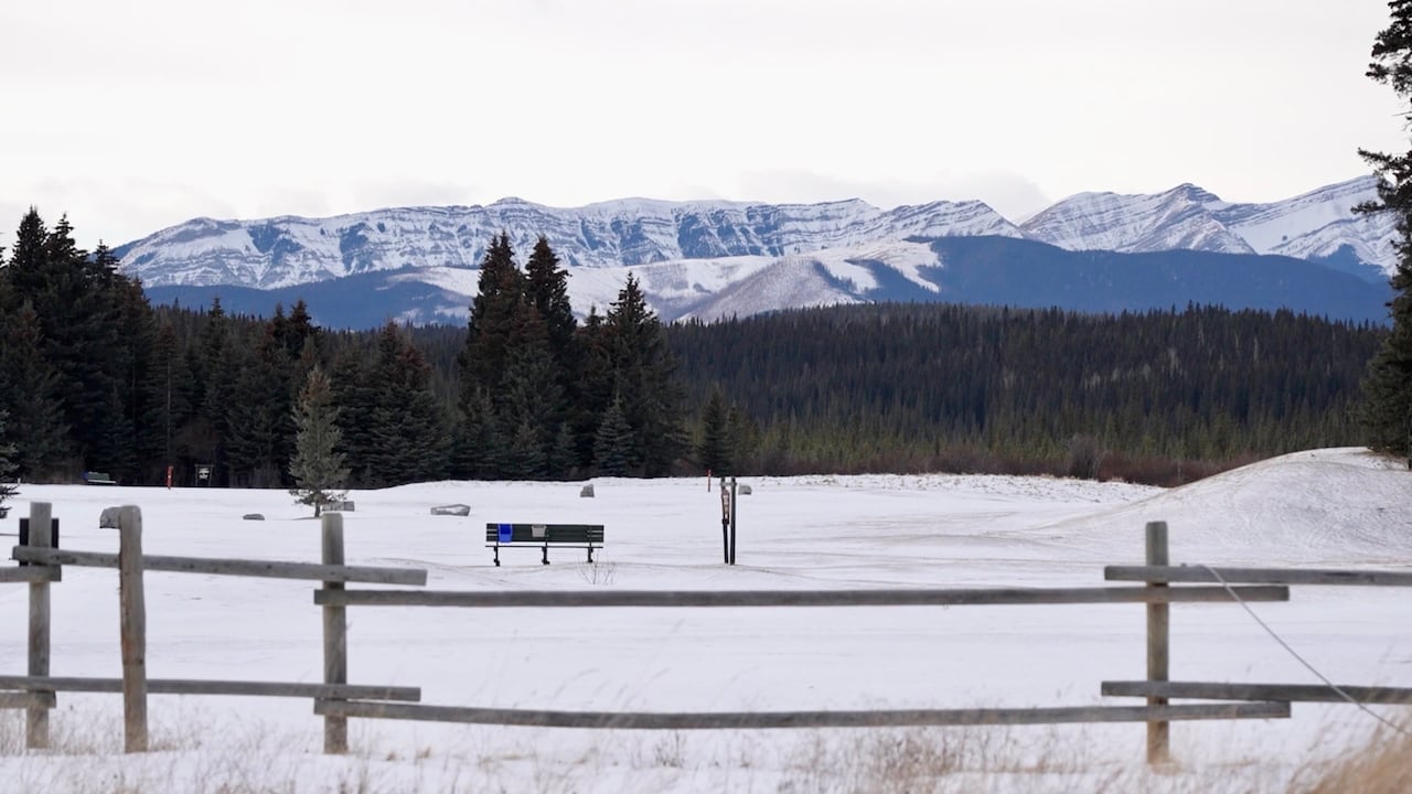 A bench on a snowy ground overlooking the mountains.