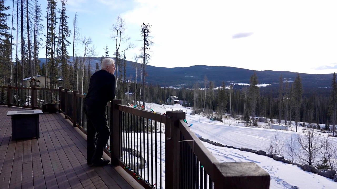 Man standing on a balcony overlooking snowy mountains.