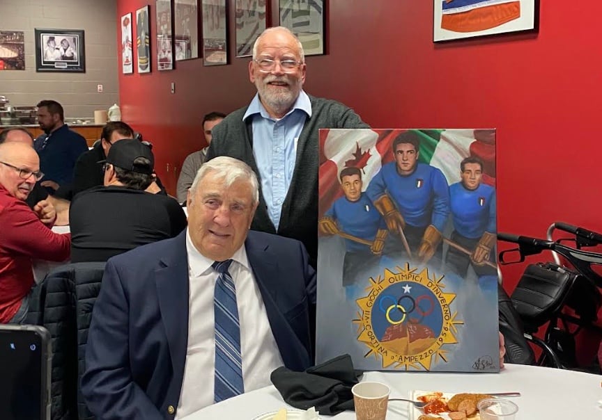 Former hockey player wearing suit, presented with Italian-Canadian painting featuring three hockey players.