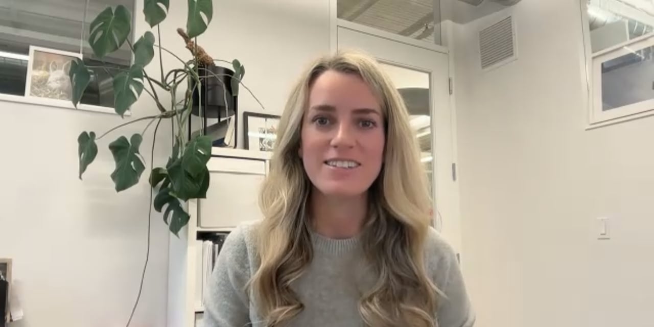 Woman in a grey sweater looks sits at a desk.