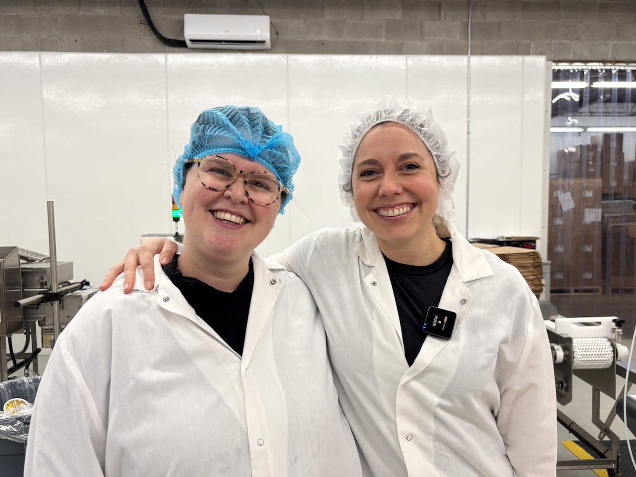 Alanmah Minarsky and Margaret Coons in hair nets and lab coats with a facility backdrop