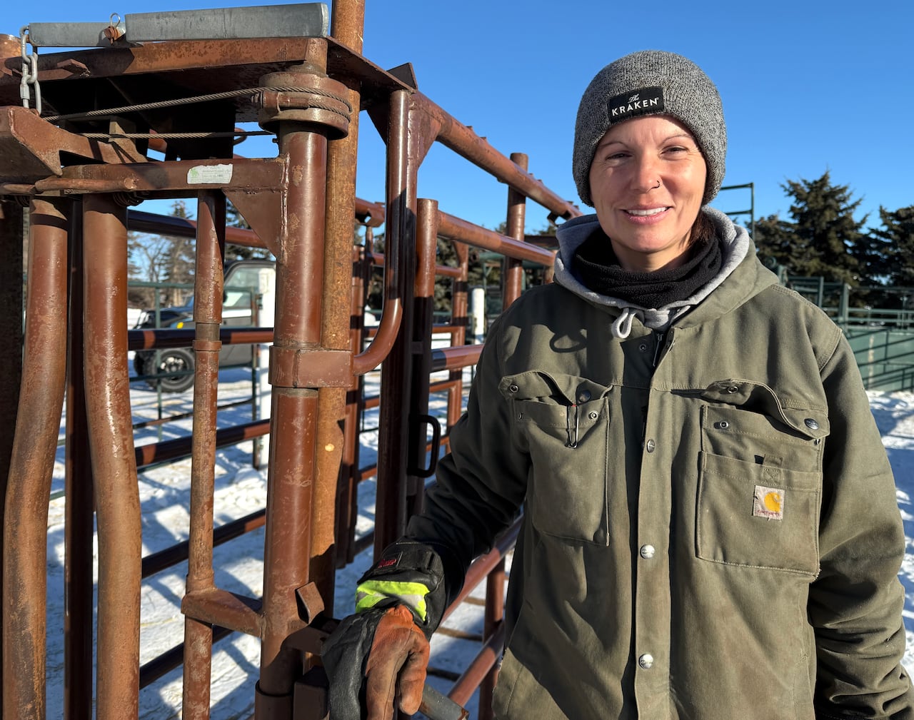 A woman in winter working clothes leans against a cattle chute.