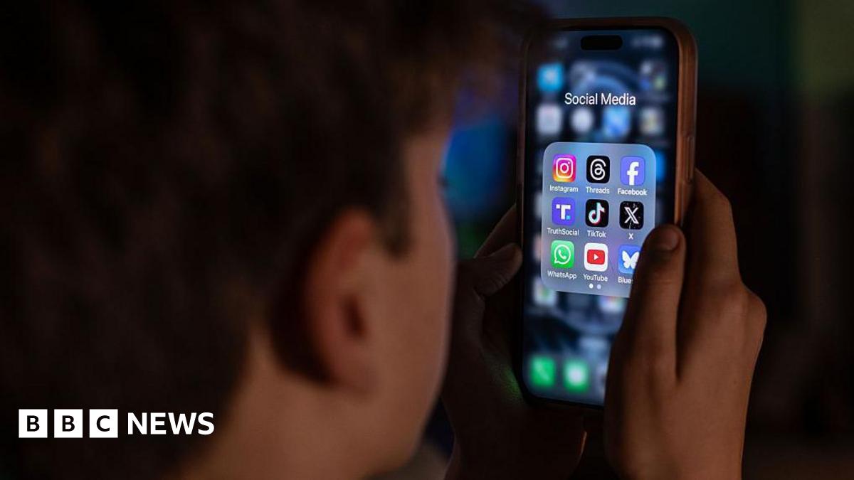 Tight close up of a teenager with his back to the camera, looking at a brightly lit smartphone screen with icons of social media ppas