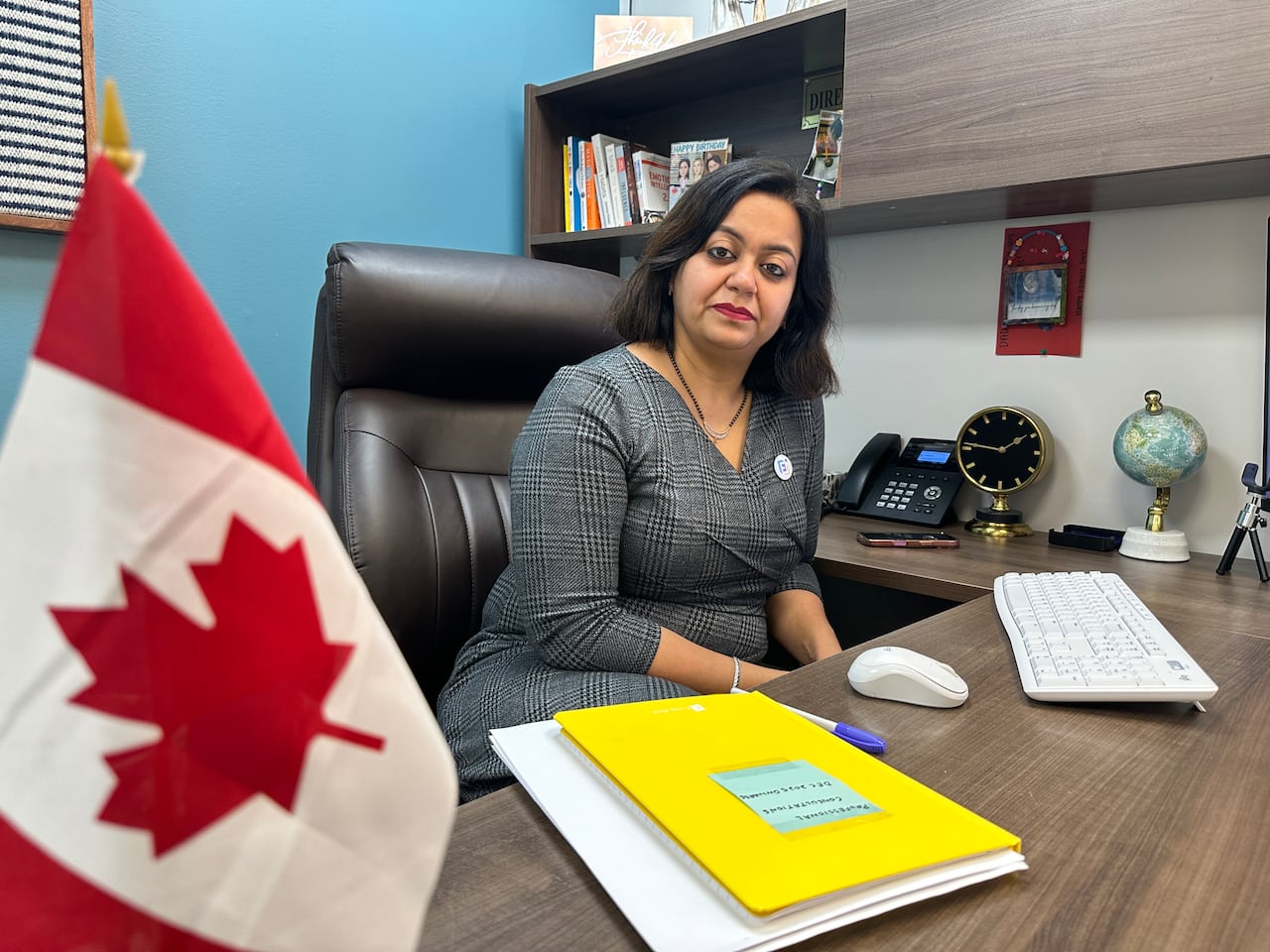 A woman sitting at the desk with a canadian flag in the left corner.