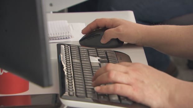A man in a blue blazer stands in his office, as a banner with the "MGEU" logo is situated some distance behind him.