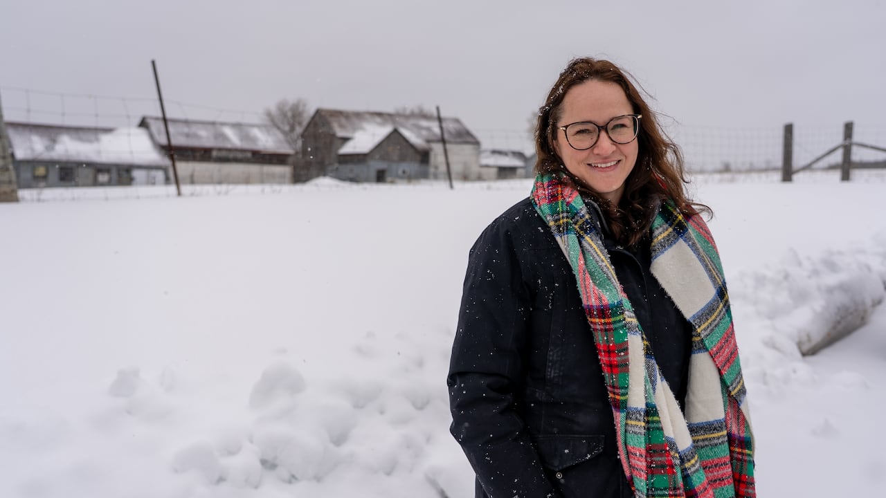 A woman in a colourful scarf in the snow with a barn in the background