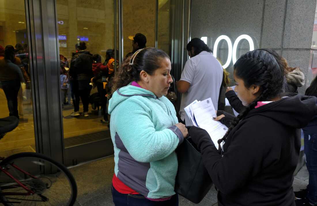 Two women look over their documents by a line snaking around the block outside the San Francisco Immigration Court in 2019.