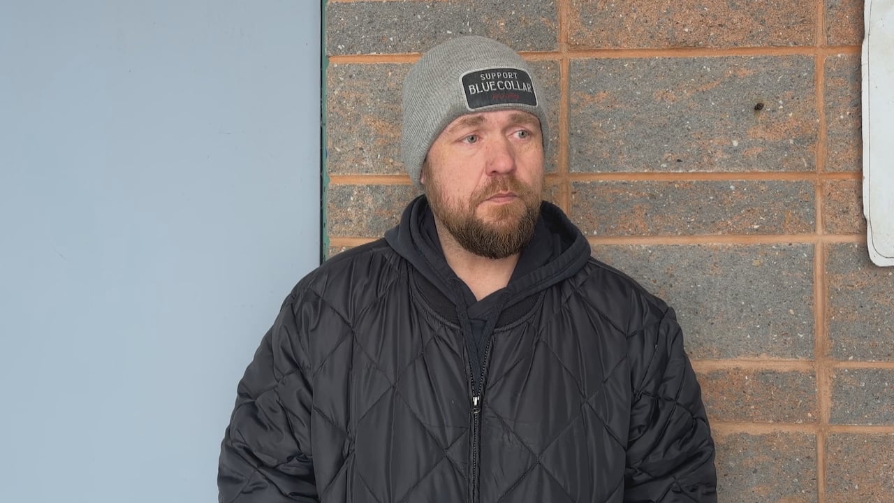A man wearing winter clothing stands in front of a brick wall.