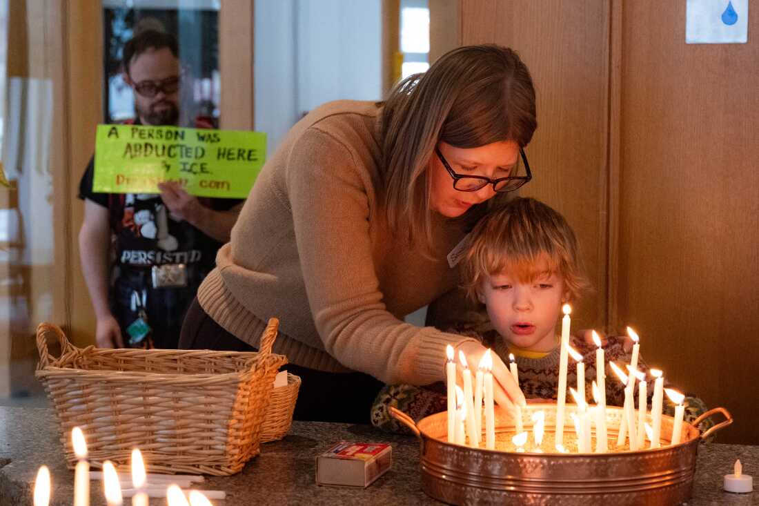 Samantha Heaton and her son Elliot Heaton, 7, light a prayer candle during service at Our Saviour's Lutheran Church as Samuel Hesla holds a sign marking an abduction by ICE at the church in Minneapolis on Sunday.