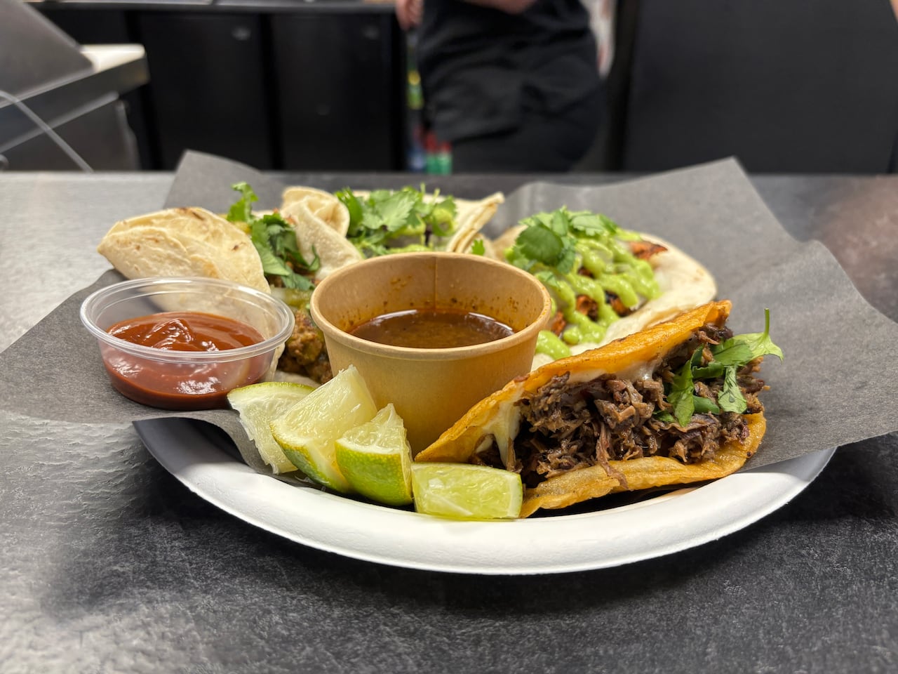 Four different kinds of meat tacos laid out on a plate with two sauces and slices of lime