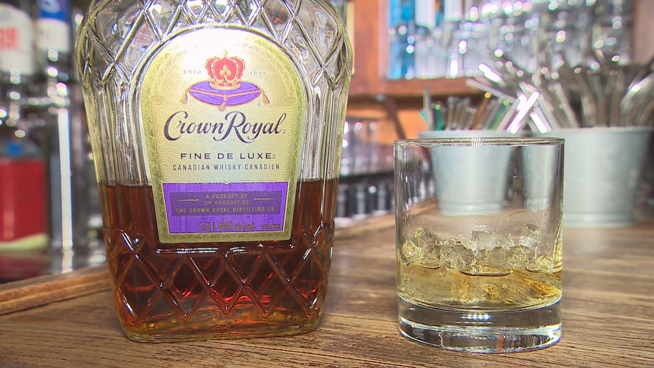 A bottle and glass of Crown Royal whisky is displayed on a wooden bar