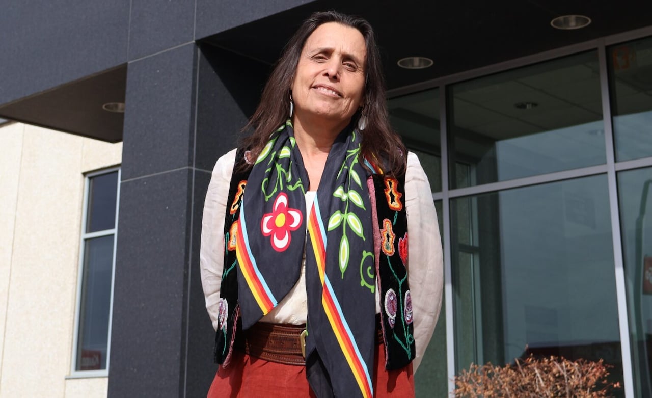 Woman wearing floral scarf, smiling and standing in front of building.