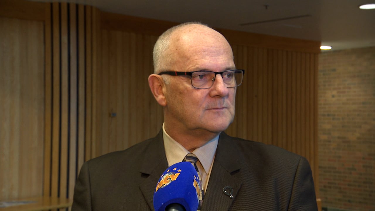 A man wearing a suit stands behind a microphone.