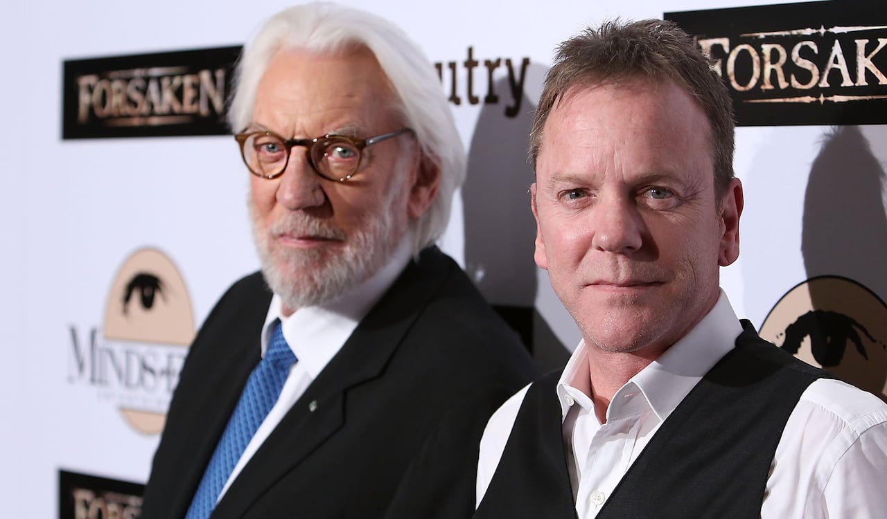 Two men, one white-haired with glasses, pose on a red carpet