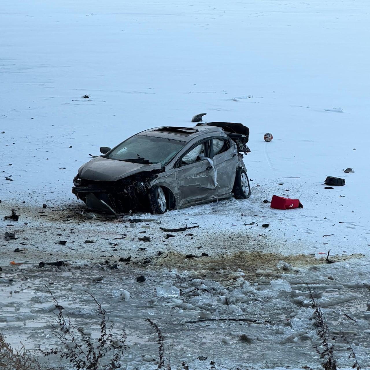A damaged car on ice under a bridge