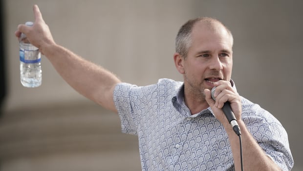 A man in a blue suit speaks into a microphone.
