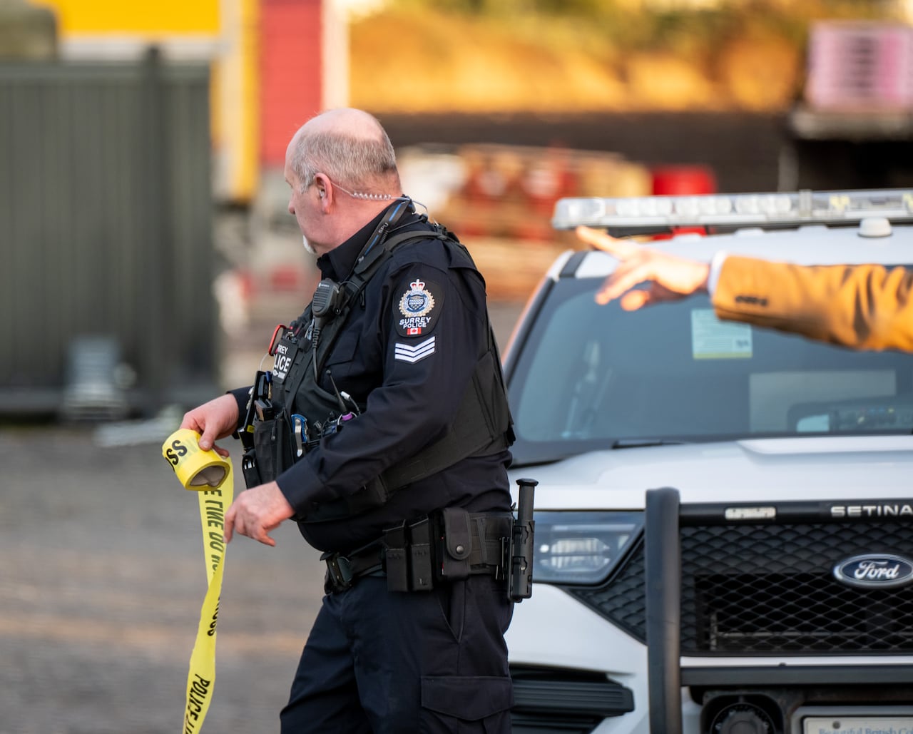 A police officer rolls up crime tape as someone points off in the distance.