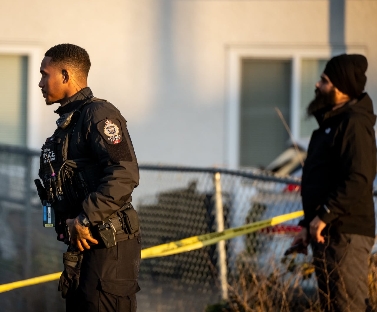 A police officer and bystander look on behind crime tape.